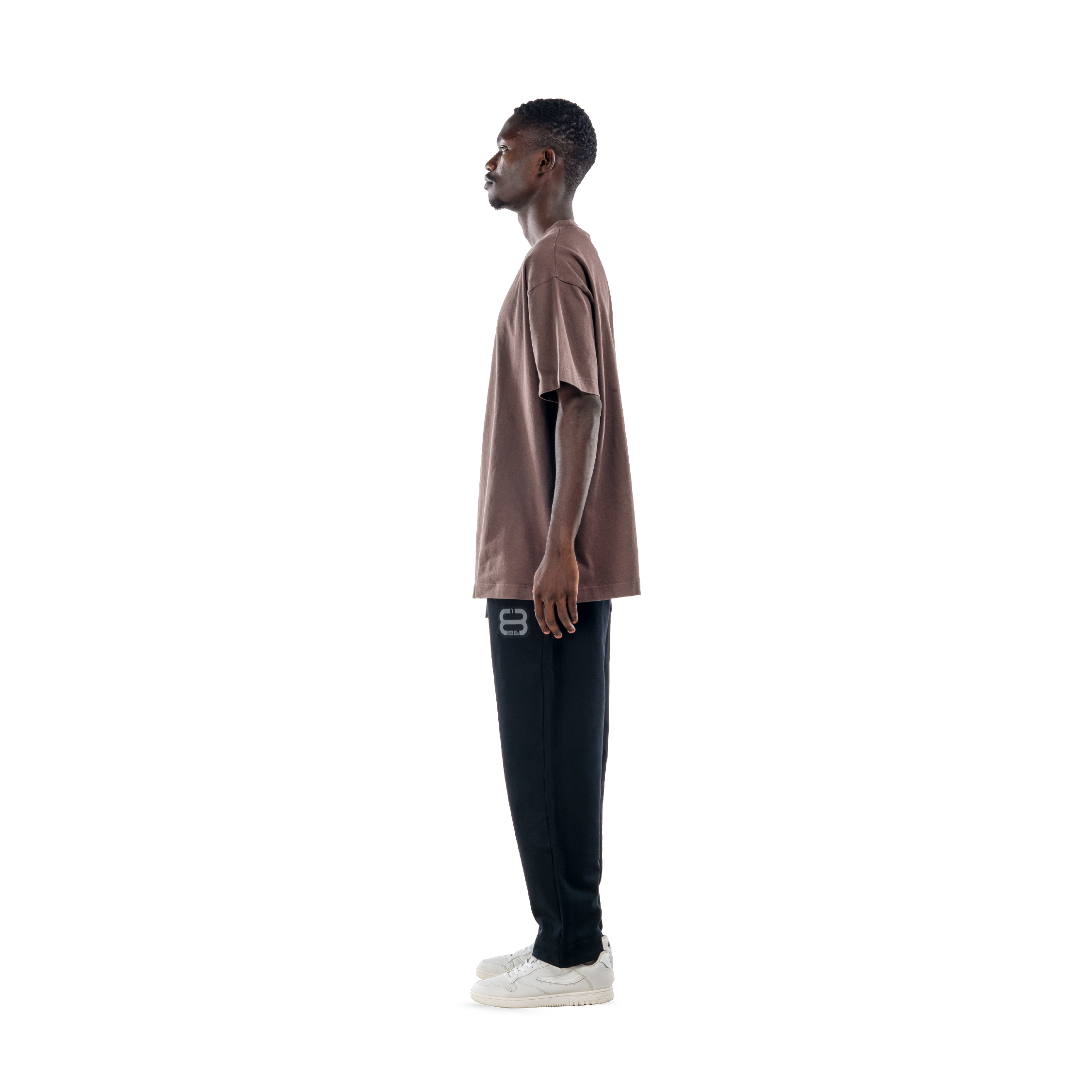 model wears ash brown t-shirt with black sweatpants and white shoes. side view.