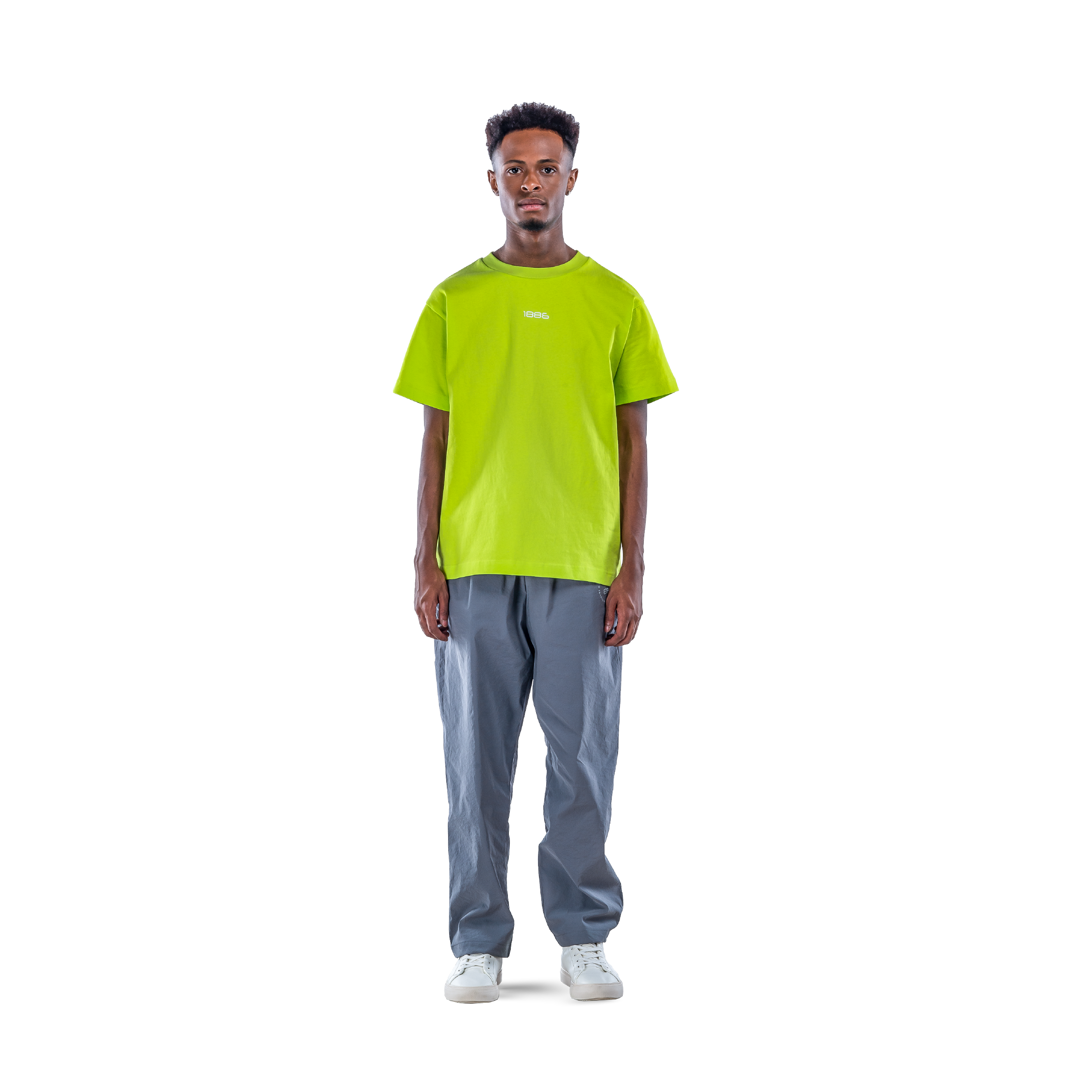 model wears neon green t-shirt with black sweatpants and white shoes. front view.
