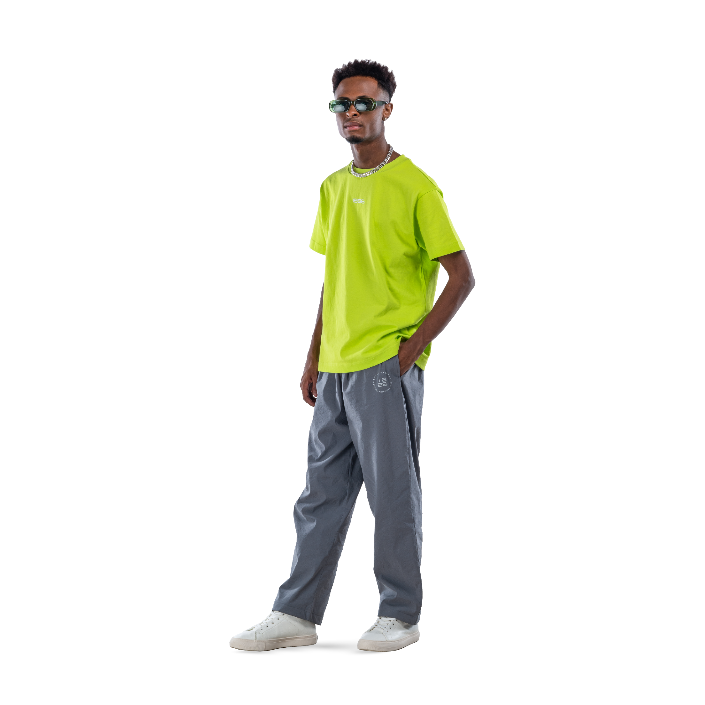 model wears neon green t-shirt with black sweatpants, sunglasses and white shoes. front view.