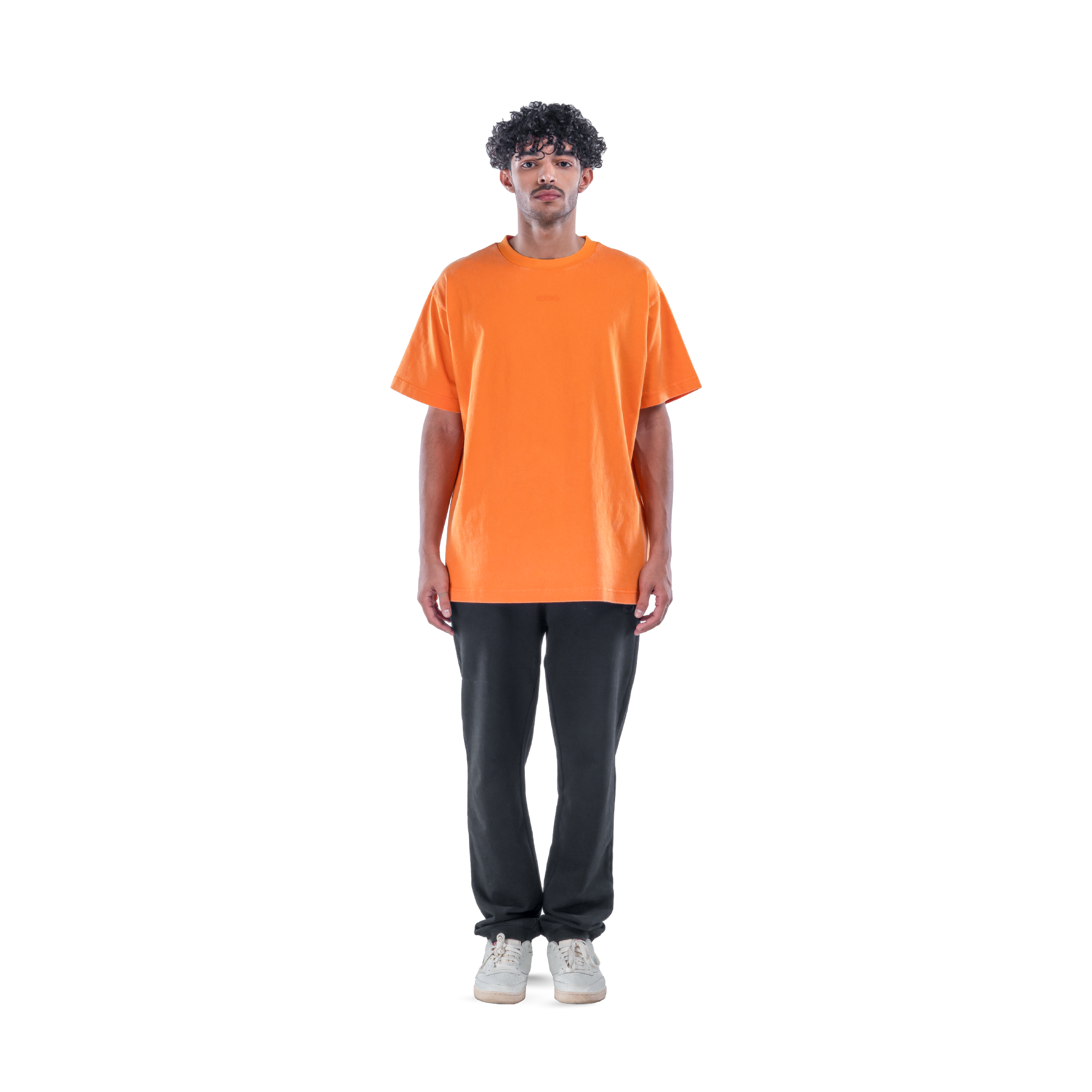 model wears orange t-shirt with black sweatpants and white shoes. front view.