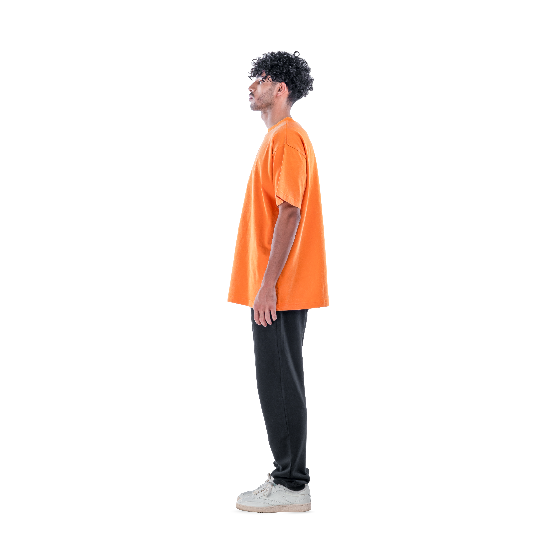 model wears orange t-shirt with black sweatpants and white shoes. side view.