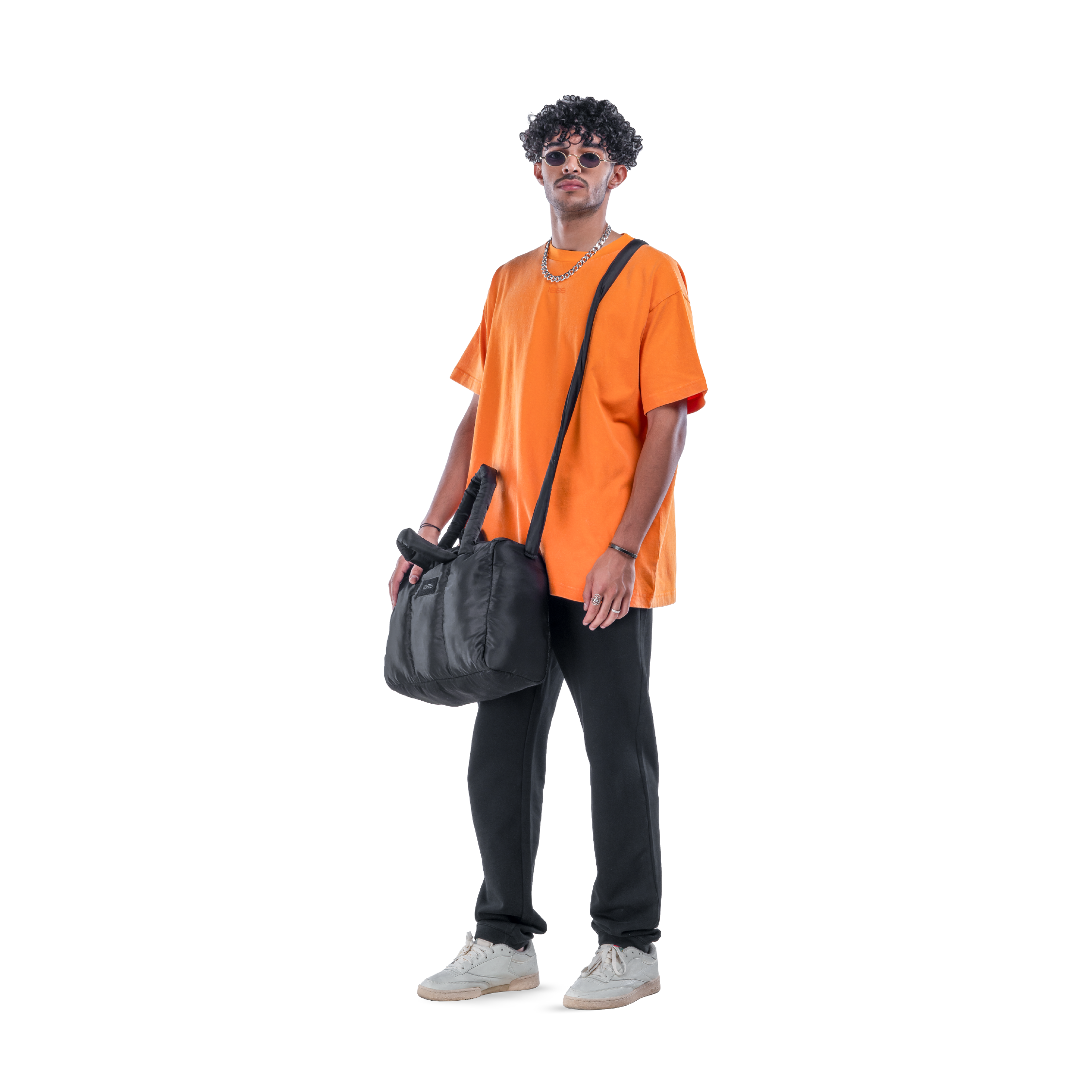 model wears orange t-shirt with black sweatpants, sunglasses and white shoes. front view.